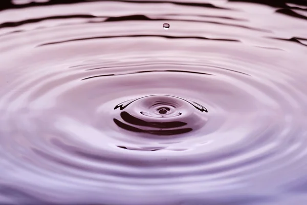 Rippled water surface with water drop above in purple colors - time abstract