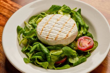 Lezzetli ızgara yumuşak peynir yeşil salatada, domatesler beyaz tabakta