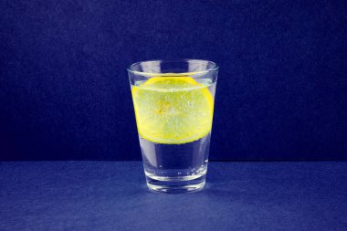 Refreshing mineral water with slice of lemon fruit in glass on dark blue background
