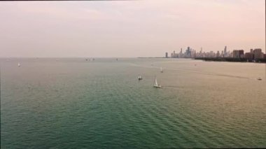 Gün batımından önce Chicago ufuk çizgisi ve ufukta yükselen binalarla birlikte yelkenliler yüzerken Michigan Gölü 'nde kayarak geçen bir motorlu tekne görüntüsü..
