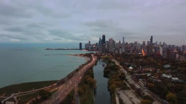 Şikago 'nun hava manzarası Lincoln Park' taki South Lagoon 'da trafik ve şehir ışıkları bulutlu bir akşamda gün batımından hemen önce açılmaya başlarken güzel görünüyor.