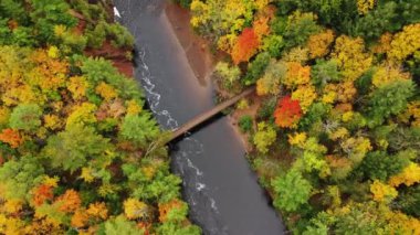 Copper Şelalesi 'ndeki Bad River' ı takip eden yaya köprüsünün üzerinden güzel bir hava manzarası var. Renkli yeşil, sarı ve turuncu yapraklar sonbaharda Mellen, Wisconsin 'de nehir kıyılarını kaplıyor.