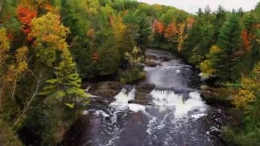 Patates Şelalesi 'nin yukarısında yeşil, kırmızı, sarı ve turuncu ağaç yapraklarıyla yükselen güzel hava manzarası ya da sonbaharda bulutlu gökyüzü ile nehri çevreleyen yapraklar..