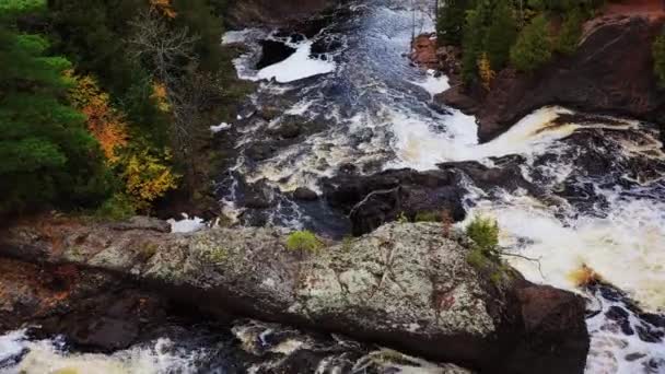 上流の滝、緑、黄色、オレンジ色の木の葉や秋に川の岸に沿って紅葉と岩や滝を飛んで美しい空中ビュー. — ストック動画