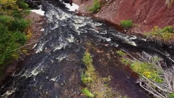 Laag niveau of hoogte vlucht naar beneden kijkend over de rotsachtige rivierbedding en wildwater stroomversnellingen op de Aardappel Rivier net onder de watervallen met rood vuil rotsachtige kliffen en bomen langs de oevers van de rivier. — Stockvideo