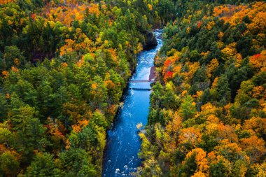 Copper Falls 'taki Bad River' ın parlak mavi sularından geçen yaya köprüsünün güzel seyahat havası. Sonbaharda Mellen, Wisconsin 'de nehir kıyısında renkli bir sonbahar yeşilliği var..