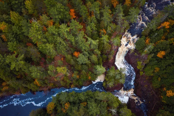Beautiful look down aerial over Brownstone Falls on Tyler Forks river as it merges with the Bad River with colorful fall foliage and red rock lining the river banks in autumn at Copper Falls park.