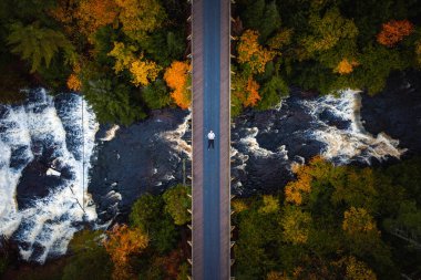 Güzel bir sonbahar, Ontonagon Nehri 'ni geçen terkedilmiş demiryolu köprüsüne uzanmış bir adamın seyahat antenine bakın ve aşağıdaki ağaçlardan oluşan şelaleyle çevrili Agate Şelalesi..