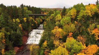 Ontonagon Nehri 'ni geçen terk edilmiş demiryolu köprüsünün panoramik havasını ve aşağıdaki Agate Şelalesi' nin manzarası yağmurlu sonbaharda ağaçlardan oluşan bir ormanla çevrili..