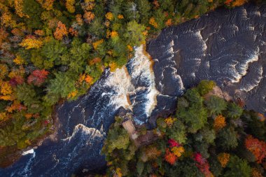 Ağaçlardaki yeşil, kırmızı, turuncu ve sarı yapraklarla çevrili Tahquamenon Şelaleleri 'ndeki alçak şelale şelalelerinin ve beyaz su akıntılarının güzel havadan çekilmiş fotoğraflarına bakın..