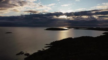 Sugarloaf Dağı 'nın yukarısında güneşin bulutların arasında parladığı ve sudan yansıyan Presque Adası ve Superior Gölü' ndeki adalara bakan güzel bir gündoğumu manzarası..