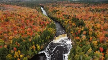 Havadan aşağıya güzel bir bakış geliyor Tahquamenon şelalesinden şelaleye doğru çekiliyor ve aşağıdaki turist izleme platformu yemyeşil ağaçlar ve sonbahar yaprakları ile çevrili..