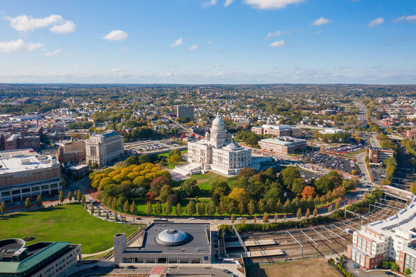Providence, RI - October 21st, 2020: The historic Rhode Island State House with its large dome and white masonry exterior rests on top of the hill surrounded by autumn colored trees in downtown.