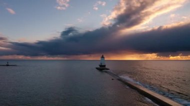Dalgalar yükselirken ve bir kuş Ludington deniz feneriyle birlikte mavi ve turuncu renkli bir günbatımı gökyüzünün önünde uçarken günbatımının güzel günbatımı duvarının üzerinde dönüyordu..