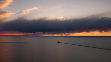 Beyaz renkli Ludington dalgakıran fenerinin önünde mavi ve turuncu gökyüzü ve Michigan Gölü 'nün suyuna yansıyan bulutlarla güzel bir günbatımı havası süzülüyor.