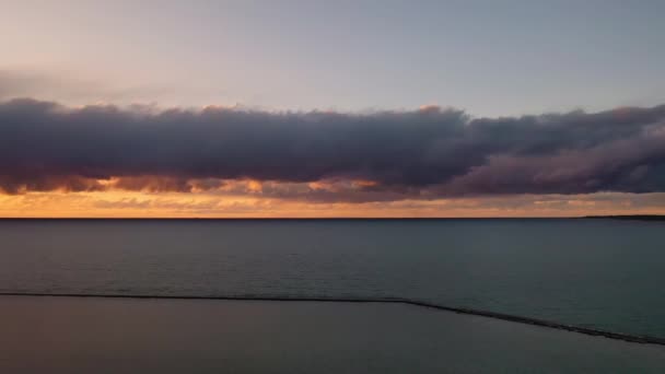 白い色のラディントン防波堤灯台と青いオレンジの空と雲の上の周囲の海岸線の美しいパニング夕日ミシガン湖の水を反映して — ストック動画