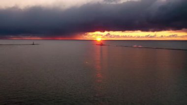 Gün batımının güzel havası beyaz renkli Ludington dalgalı deniz fenerine doğru dönüyor pembe, sarı ve turuncu gökyüzü ve güneş ve bulutlar Michigan Gölü 'nün sakin sularını yansıtıyor..