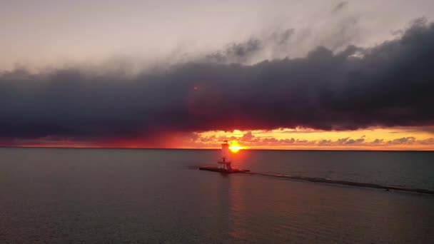 ミシガン湖の水を反映し カラフルなピンク オレンジと黄色の色で空と雲を照らす太陽とルディントン防波堤灯台の美しいパノラマ — ストック動画
