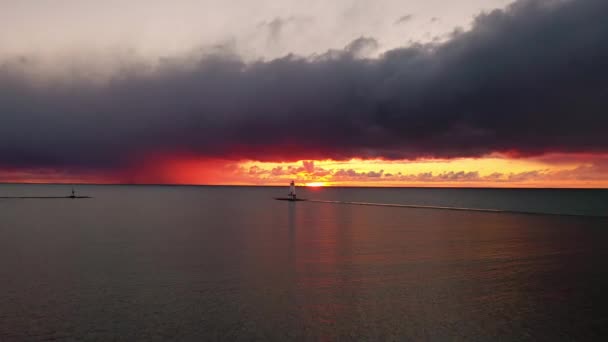 ミシガン湖の水を反射し カラフルなピンク オレンジ 黄色で空と雲を照らす太陽とルディントン防波堤灯台の美しいパンニング — ストック動画