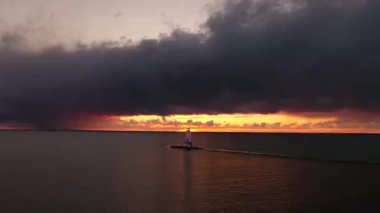 Beyaz renkli Ludington deniz fenerinin güzel günbatımı antenleri pembe ve turuncu gökyüzü ve yukarıdaki bulutlar Michigan Gölü 'nün sakin sularına yansıyor..