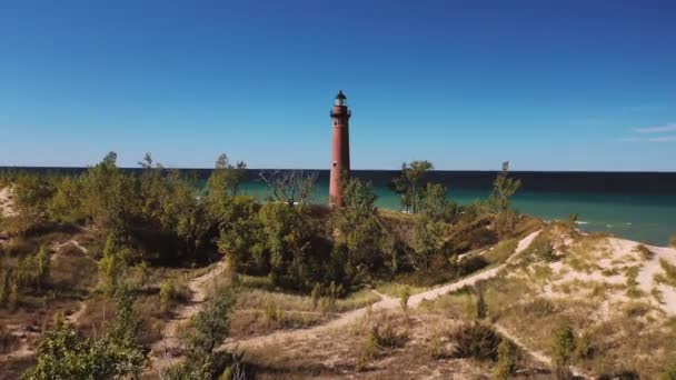 美丽的空中风景俯瞰着密西根湖沿岸的一座小灯塔 它坐落在植被和绿树成荫的沙丘之间 蓝蓝的天空笼罩着一片蓝天 — 图库视频影像