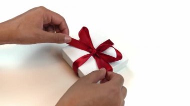 Beyaz bir arka planda beyaz bir mücevher hediye kutusuna sarılı kırmızı kurdele takan Afrikalı Afrikalı Amerikalı bir kadının elleri tatil ya da Noel 'de yakındır..