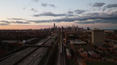 Chicago, IL - 15 Ekim 2020: Bir Metra treni gün batımında yakınlardaki otoyolda trafik akarken şehir merkezindeki ufuk çizgisine doğru yola çıkıyor..