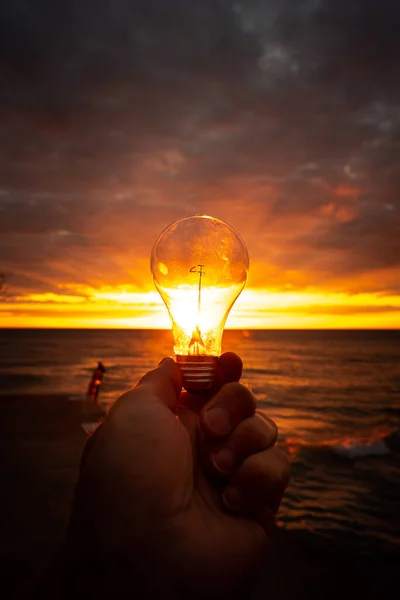 Мужчина Протягивает Ясную Лампочку Перед Красочным Восходом Солнца Над Озером — стоковое фото