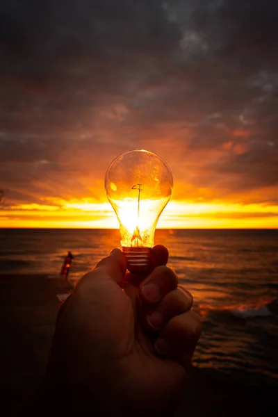 Hombre Sostiene Una Bombilla Clara Frente Colorido Amanecer Sobre Lago — Foto de Stock