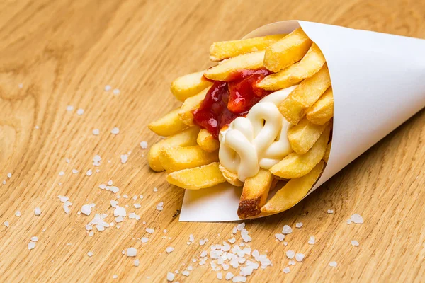 French fries in bag with salt on wood — Stock Photo, Image