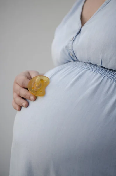 Pregnant woman in light blue denim dress holding pacifier — Stock Fotó