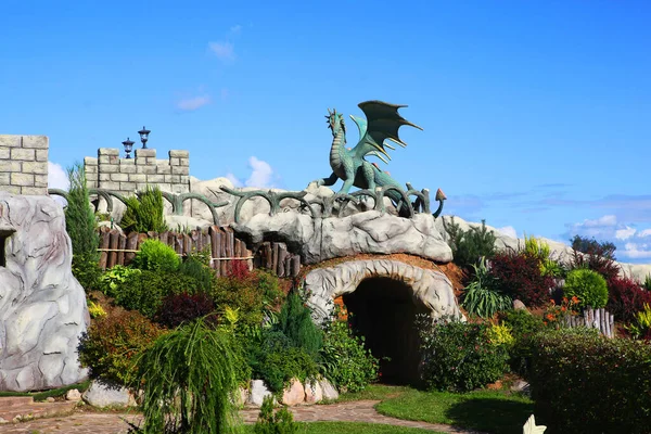 Fantasy landscaping with a dragon, cave and castle walls.