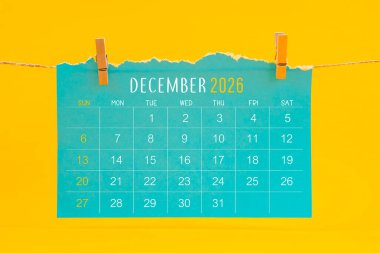 Aralık 2026 takvim yırtılması sarı zemin üzerinde kahverengi halatla asıldı.