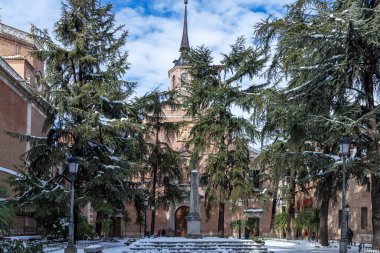 Alcala de Henares şehrinde güneşli bir günde arka planda Saint Bernard manastırı ve bulutlu mavi gökyüzü ile kar yağışı sonrası bernardas meydanının yatay görüntüsü