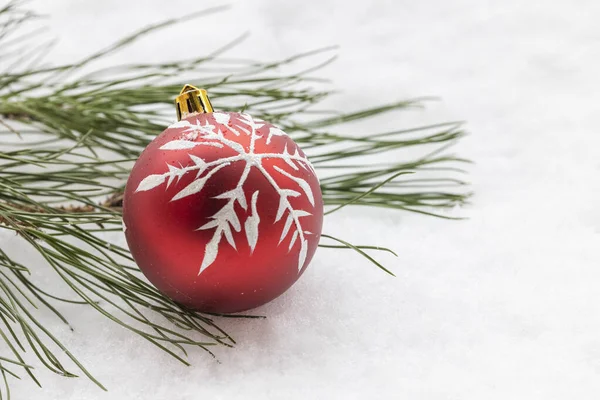 Kırmızı bir noel ağacı topunun önü ve arka planda çam dalı