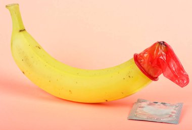 Pembe arka planda kırmızı prezervatif ve muz. Güvenli seks konsepti. Dünya AIDS Günü konsepti.