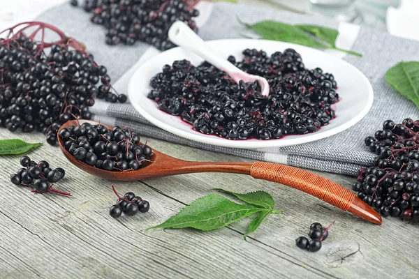 Delicious homemade black elderberry syrup and bunches of black elderberry with green leaves on wooden desk. Elderberry syrup immunity boosting for flu season.