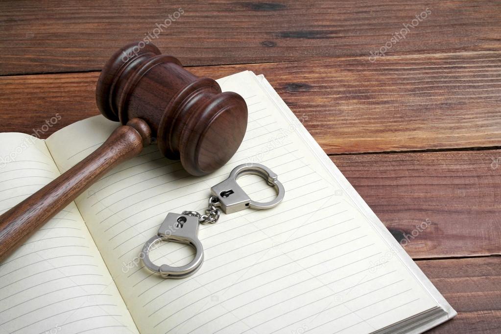 Wooden gavel, open book and handcuffs on wooden background