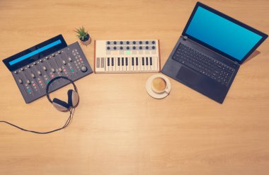 Midi klavyesinin üst görüntüsü, kontrol yüzeyi ve tahta zemindeki dizüstü bilgisayar. ev müziği stüdyo ekipmanı konsepti