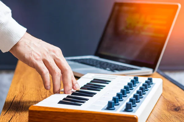 male producer, musician hand playing midi keyboard for arranging a song on laptop computer in home studio