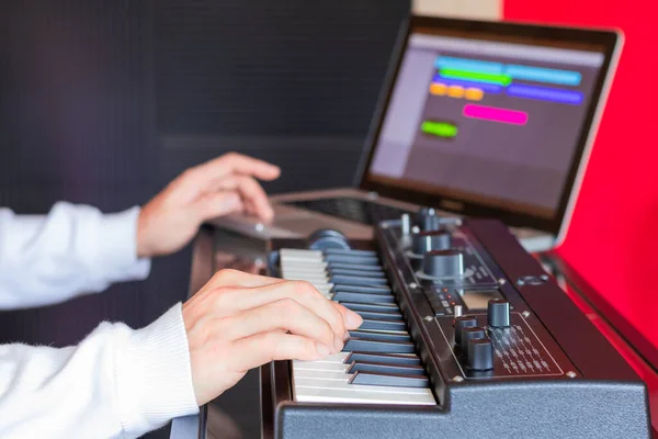 male music composer hands playing synthesizer keyboard for recording midi tracks on laptop computer. music production technology concept