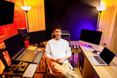 Genç Asyalı erkek yapımcının portresi kayıt stüdyosunda oturuyor.