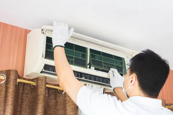 asian man remove dust filter for cleaning air conditioner system in living room