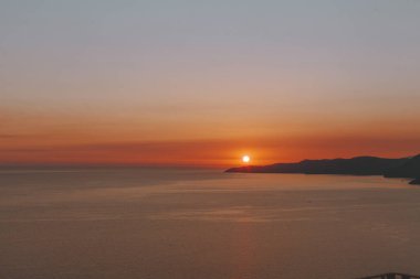 Sun going down behind the hills and sea. Romantic sunrise or sunset over sea with hills in background.