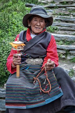Tibet 'teki Everest Ana Kampı' nın yakınlarında, açık bir alanda duran dua tekeri ve boncuklu yaşlı Tibetli kadının tanımlanamayan portresi.