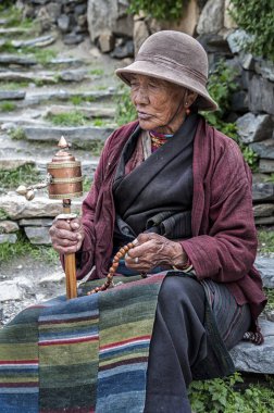 Tibet 'teki Everest Ana Kampı' nın yakınlarında, açık bir alanda duran dua tekeri ve boncuklu yaşlı Tibetli kadının tanımlanamayan portresi.