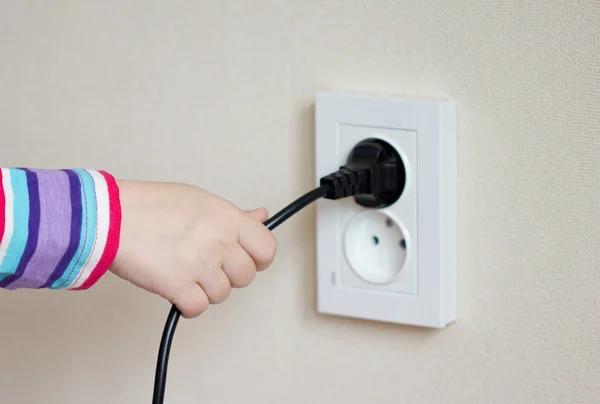 Mano del niño para tirar de un cable eléctrico de la toma de corriente — Foto de Stock