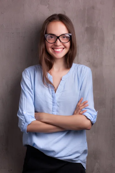 Portret van mooie gelukkig jonge vrouw met bril in de buurt van grijze achtergrond muur — Stockfoto