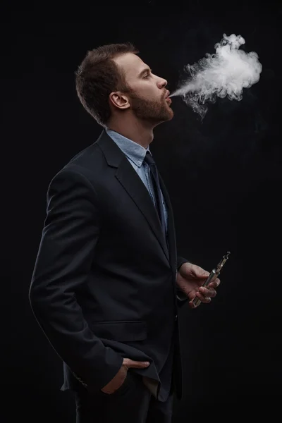 Hombre de negocios soplando humo de cigarrillo electrónico — Foto de Stock