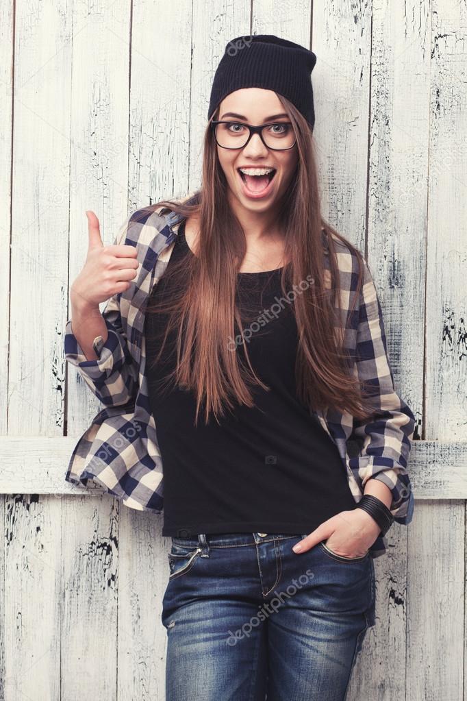Fille de hipster à lunettes et bonnet noir avec les pouces vers le haut sur le fond en bois \u2014 Image de doodko